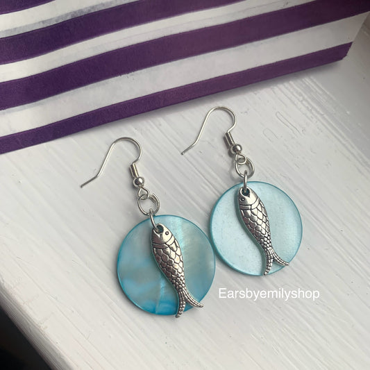 Cool beach inspired silver fish handmade drop dangle earrings on a blue sea shell disc