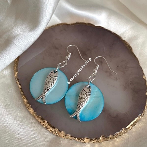 Cool beach inspired silver fish handmade drop dangle earrings on a blue sea shell disc