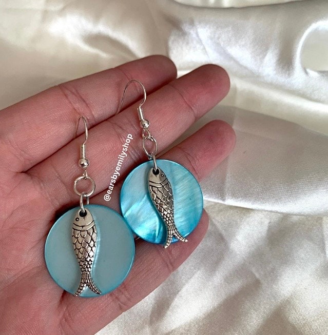 Cool beach inspired silver fish handmade drop dangle earrings on a blue sea shell disc